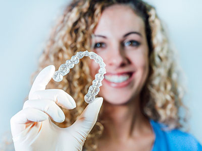 This is an image featuring a person holding up a clear dental impression tray with a smile, which appears to be used for capturing teeth impressions.