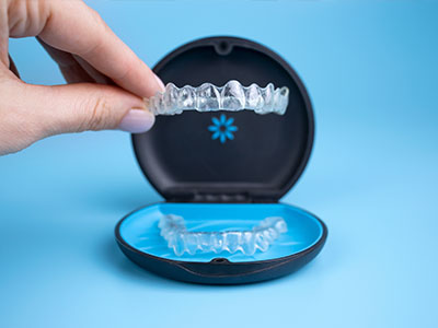 The image shows a hand holding a clear tray containing a set of dental implants next to an open box with a single implant inside, against a blue background.